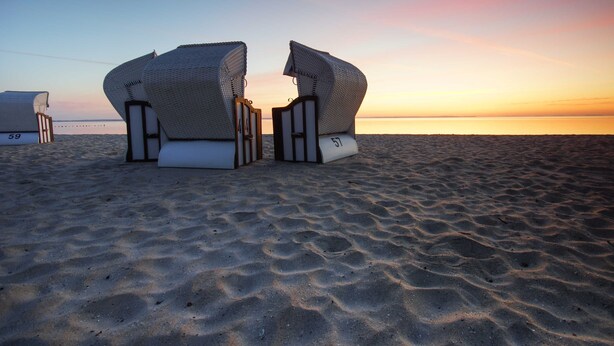 Beach chairs with numbers 59 and 57 on a sandy beach at sunset.