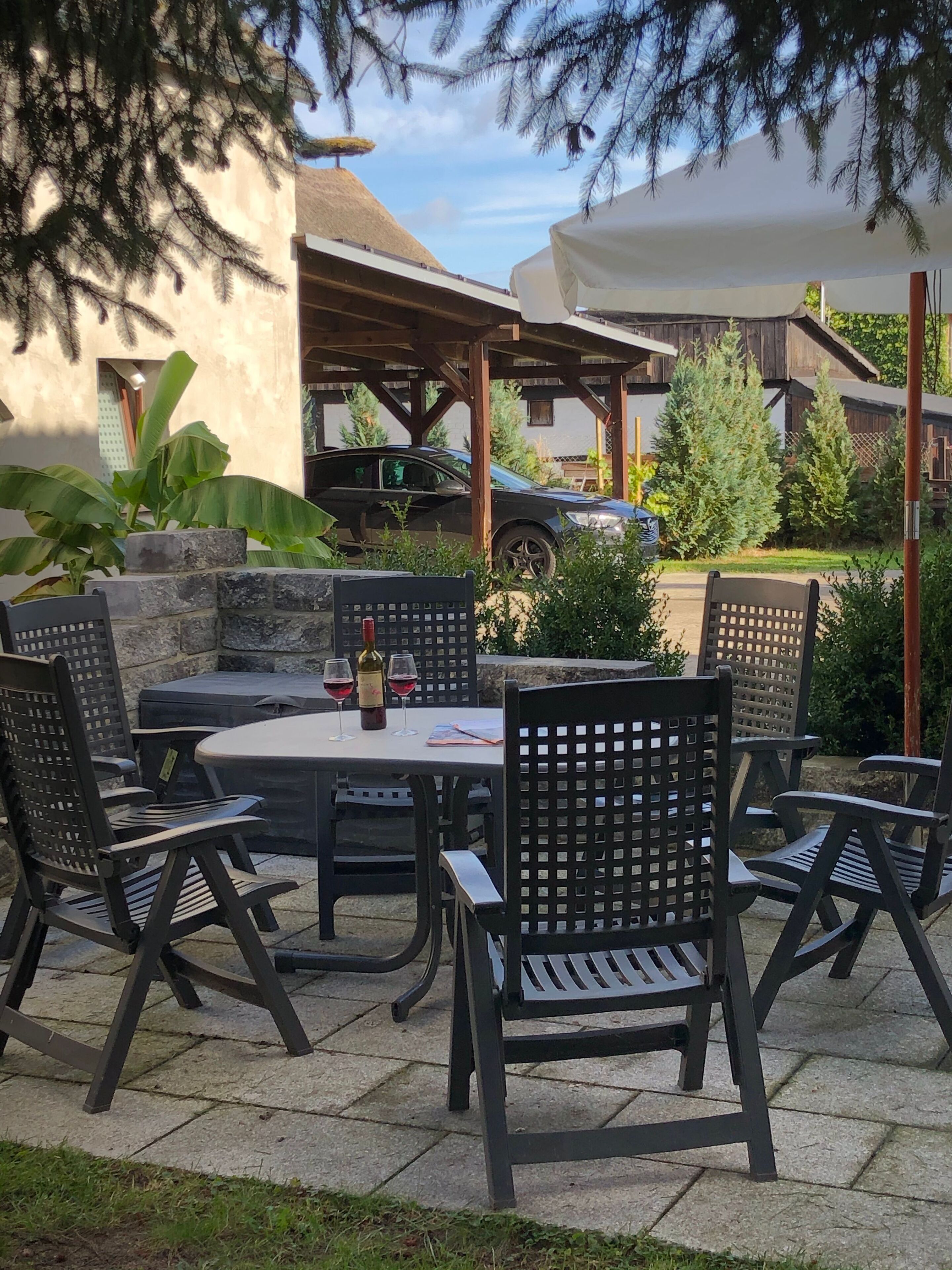 Eine Terrasse im Freien mit einem runden Tisch und sechs Stühlen, einer Weinflasche und zwei Gläsern auf dem Tisch.