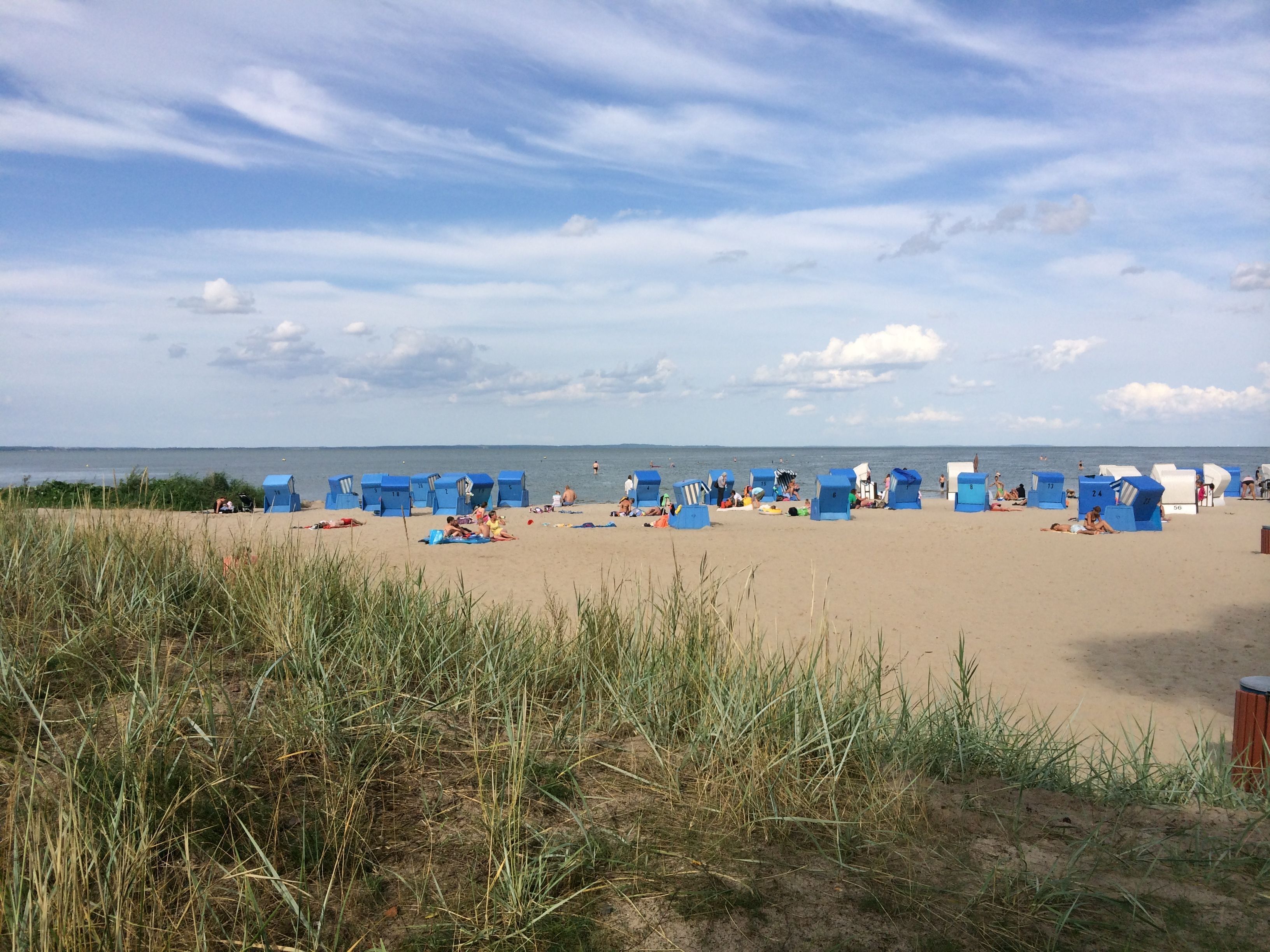 Una playa con hileras de cabañas azules y gente relajándose en la arena.