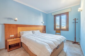 A bedroom with a wooden headboard, a single bed, a nightstand, a lamp, and a window with a view.