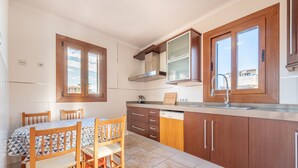 A kitchen with wooden cabinets, a built-in stove, a window, and a dining table with chairs. - Cosy Holiday Apartment with Wi-Fi, Air Conditioning and Terrace (Binissalem)