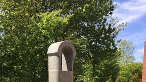 Ein Beton-Pizzaofen im Freien mit Schornstein, auf einer Terrasse mit Backsteinmauer und Bäumen im Hintergrund.