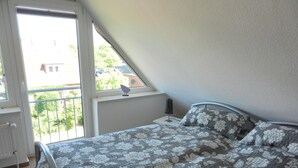 Ein Schlafzimmer mit einem Bett, einem Nachttisch, einer Lampe und einem Fenster mit Blick nach draußen.