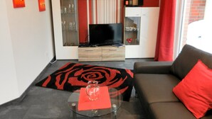 Ein modernes Wohnzimmer mit einer Couch, einem Glastisch, einem Flachbildfernseher und einer roten Akzentwand.