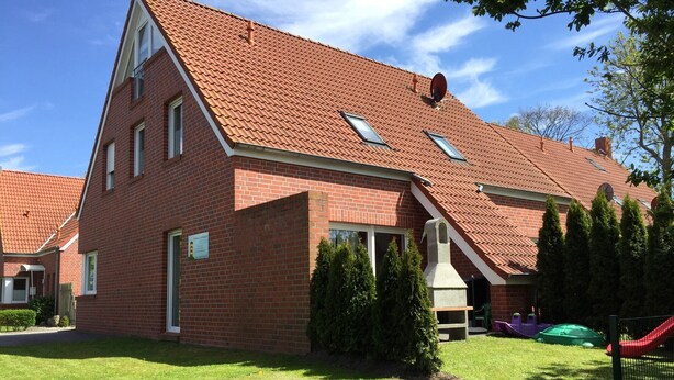 Ein rotes Backsteinhäuschen mit geneigtem Dach, Schornstein und einem kleinen Garten mit Spielbereich.