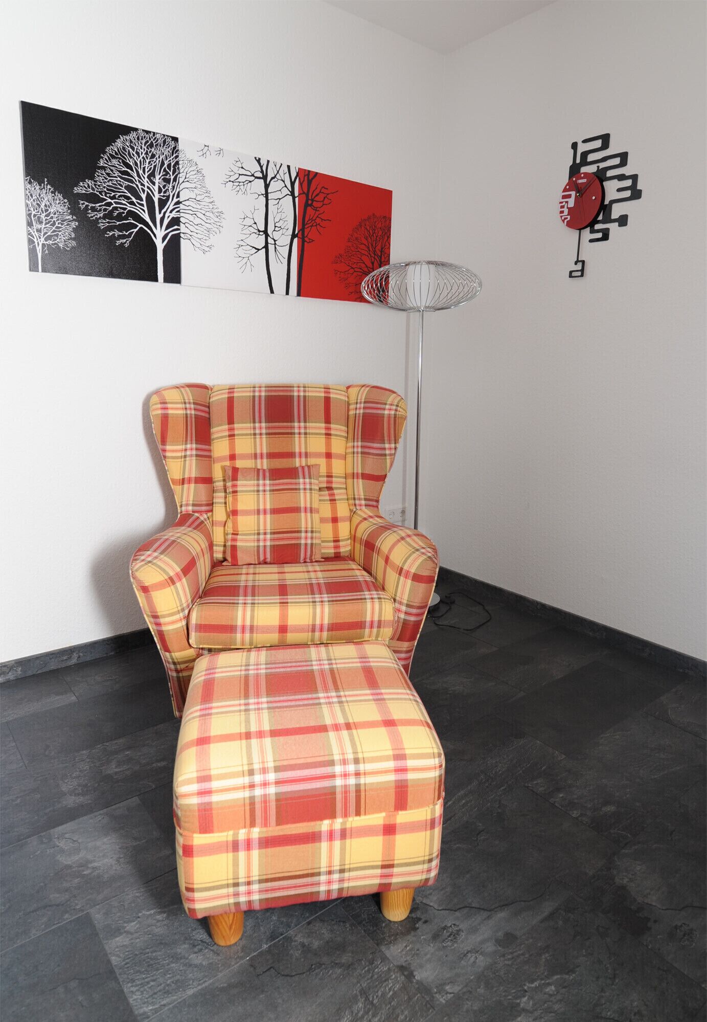 Un sillón escocés en una habitación con una lámpara de pie moderna y arte abstracto en la pared.