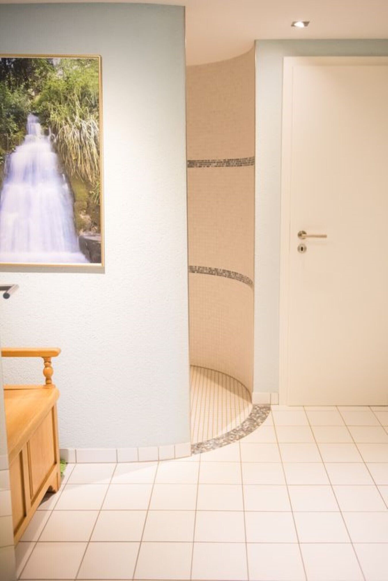 A bathroom with a shower, a wooden bench, and a framed picture of a waterfall.