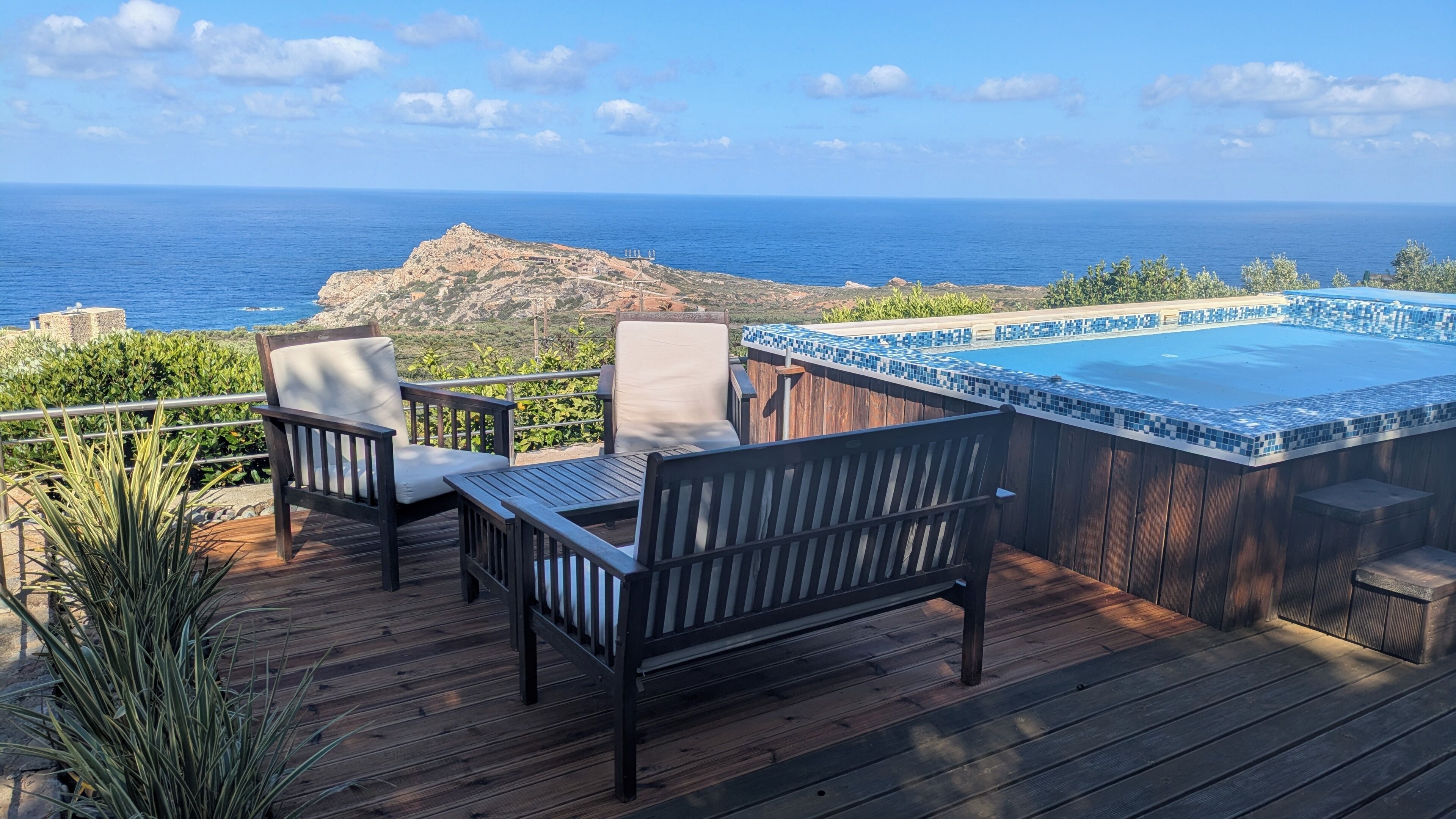 Een houten terras met tuinmeubilair, een hottub en uitzicht op de oceaan.