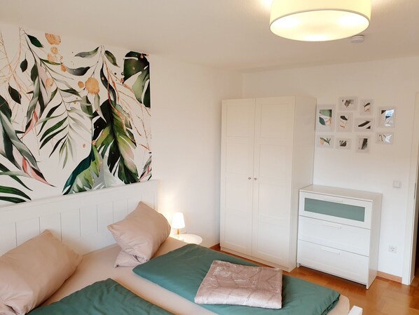 A bedroom with two beds, a wardrobe, a desk, and a wall with framed pictures.