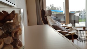Una habitación con un ventanal grande, una mesa blanca, una silla de mimbre y vistas al exterior.