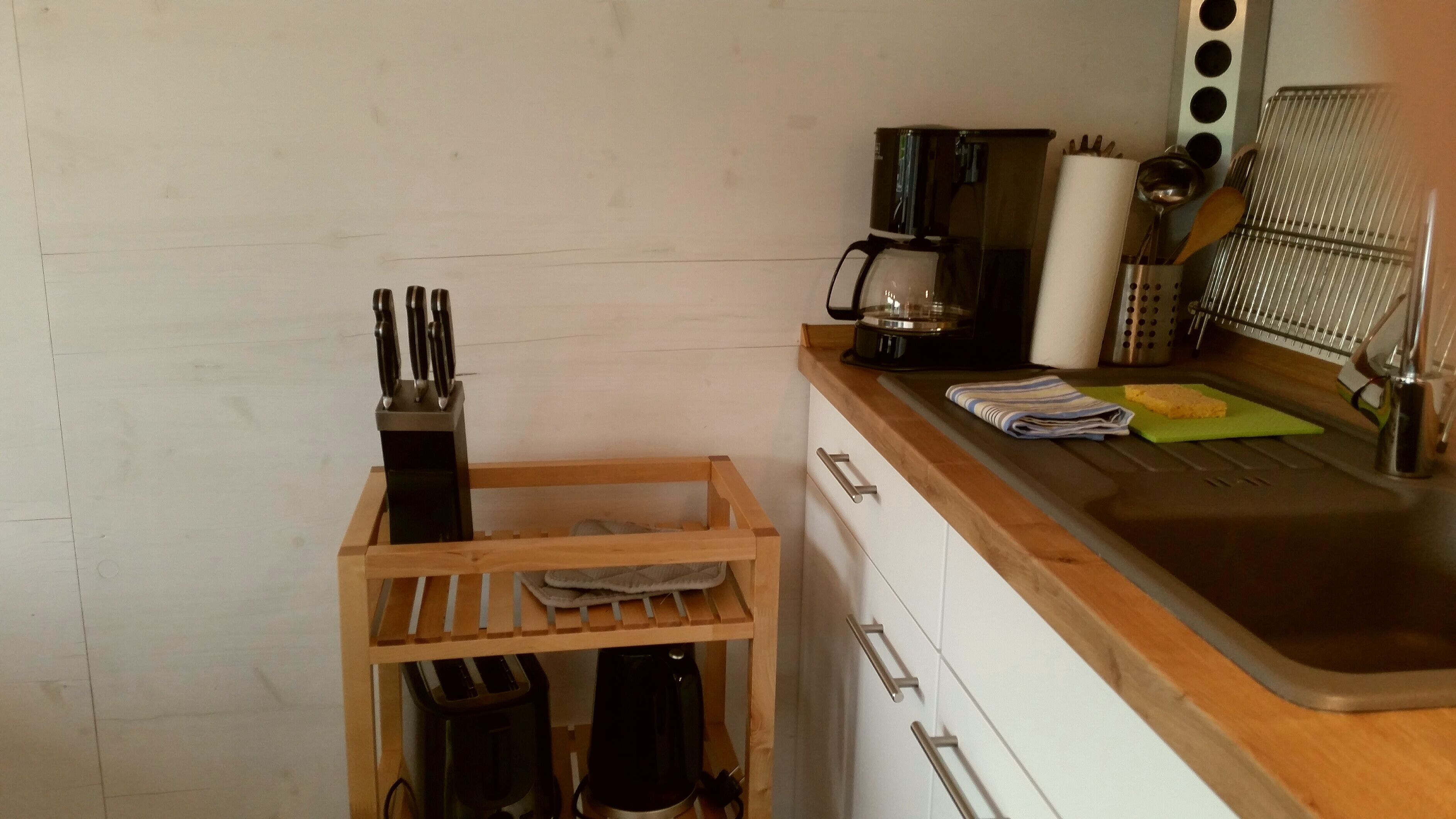 A kitchen with a wooden utensil holder, a coffee maker, and a sink.