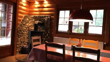 Cozy cabin-style room with a stone fireplace, dining area, and large windows offering scenic views.
