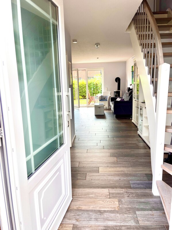 A spacious hallway with a wooden floor, a staircase, and a sliding glass door leading to an outdoor area.