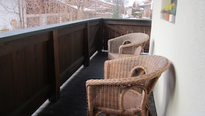 Ein Balkon mit Korbstühlen und Holzgeländer mit Blick auf ein verschneites Dorf.