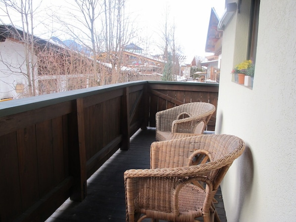 A balcony with wicker chairs and a wooden railing overlooking a snowy village.