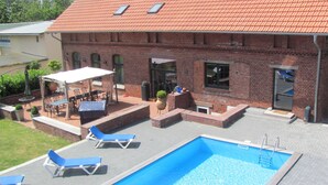 A swimming pool with lounge chairs, a covered patio area, and a brick building with a tiled roof. - Large farmhouse with pool, minutes from the beach  (Greifswald)