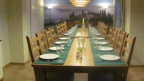 A long dining table set for a meal with chairs on both sides, a chandelier above, and a scenic mural on the wall behind. - Large farmhouse with pool, minutes from the beach  (Greifswald)
