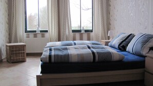 A bedroom with a bed, two windows with curtains, a bedside table, and a lamp. - Large farmhouse with pool, minutes from the beach  (Greifswald)