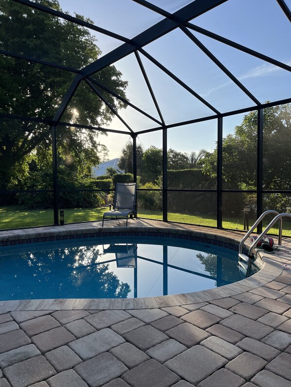 Una piscina techada con zona de terraza, rodeada por una cerca metálica y árboles.