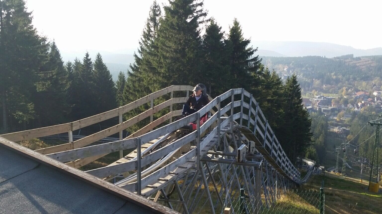 Eine Holztreppe führt zu einer Aussichtsplattform mit Metallgeländer, umgeben von Bäumen und mit Blick auf ein Tal.