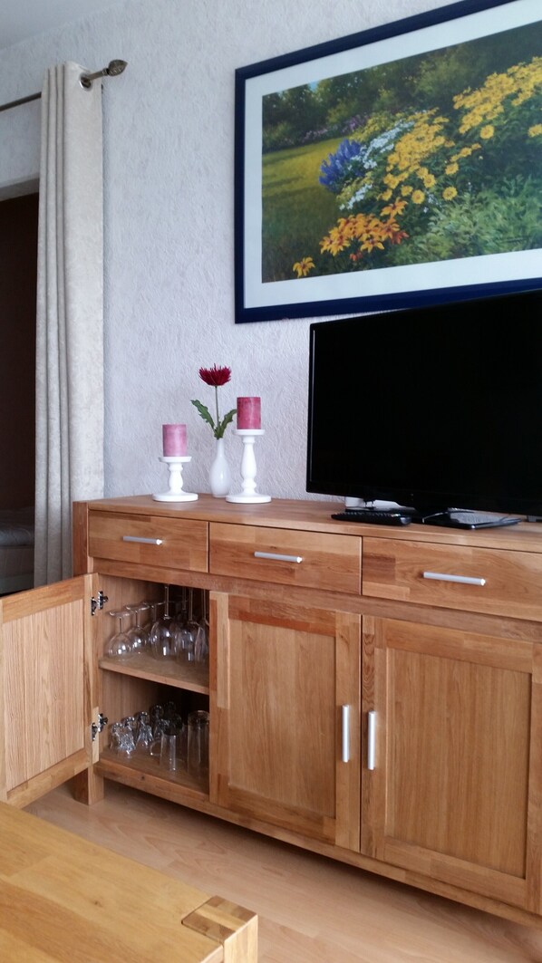 A wooden cabinet with multiple drawers and shelves, a television, and a framed picture on the wall.