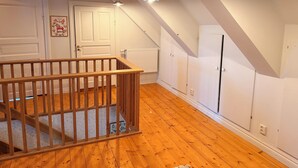 Een kamer met houten vloer, witte wanden, een houten leuning en een schuin plafond met zichtbare balken.