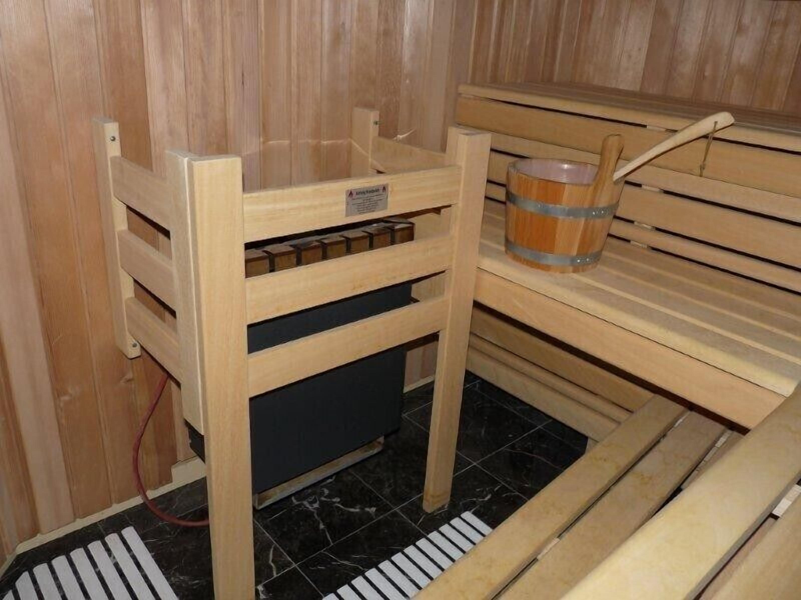 Un sauna en bois avec un banc, une table en bois avec un seau et un panneau de commande.
