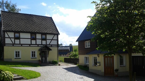 A traditional half-timbered house with a cobblestone driveway leading to a wooden gate.