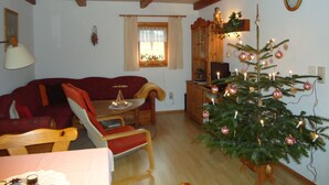 A cozy living room with a wooden ceiling, a red sofa, a wooden coffee table, and a Christmas tree.