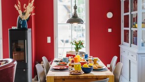 A dining area with a wooden table set for breakfast, a black refrigerator, and a red wall. - Enjoy the autumn under the thatched roof - close to the beach, comfortable, Wi-Fi, sauna, dog willk. (Glowe)