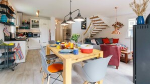 A modern kitchen with white cabinets, a wooden dining table, and a staircase leading to a loft bedroom. - Enjoy the autumn under the thatched roof - close to the beach, comfortable, Wi-Fi, sauna, dog willk. (Glowe)