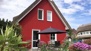 A red house with a thatched roof, a door, and a window. There is a black umbrella and a table with chairs outside. - Enjoy the autumn under the thatched roof - close to the beach, comfortable, Wi-Fi, sauna, dog willk. (Glowe)