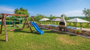 A backyard with a swing set, a blue slide, a barbecue grill, and umbrellas. - Private and secure 5000 sqm garden, pool, children's playground, only 9 km from the sea (Nedešćina)