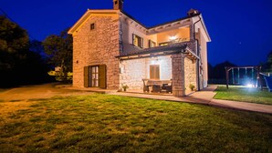 A stone house with a porch and a swing set in the yard. - Private and secure 5000 sqm garden, pool, children's playground, only 9 km from the sea (Nedešćina)