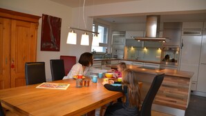 A modern kitchen with wooden cabinets, a wooden dining table, and pendant lights.