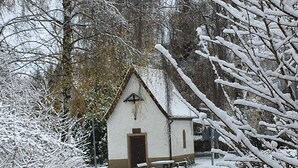 A small, snow-covered building with a simple, triangular roof and a cross on the front.