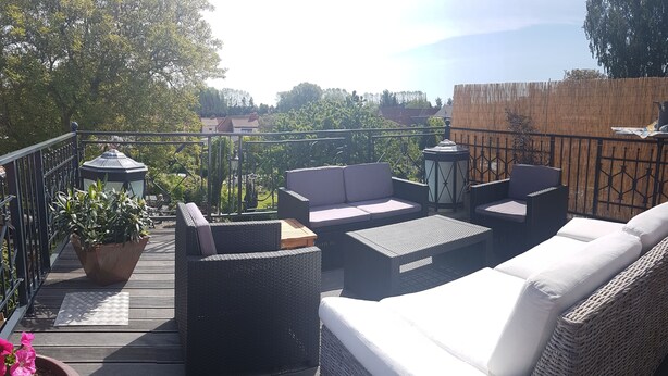 An outdoor patio with wicker furniture, a potted plant, and a view of the surrounding area. - Charming holiday apartment on the Lindenhof in Garz on Rügen (Garz auf Rügen)