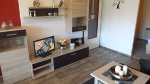 Una sala de estar moderna con un televisor de pantalla plana, armarios de madera, una cafetera y un elemento decorativo en la pared.