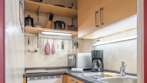 Una cocina compacta con armarios de madera, microondas integrado, cafetera y lavamanos.