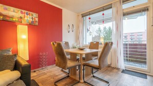Una sala moderna con una pared de acento roja, un sofá, una mesa de comedor con sillas y un ventanal con cortinas.