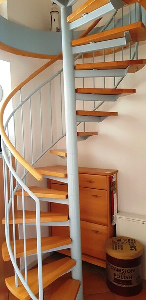 A spiral staircase with wooden steps and metal railings, a wooden cabinet, and a container of Ramison wax polish.