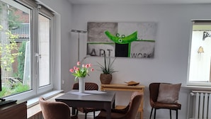 A modern dining area with a table, chairs, and a painting on the wall.