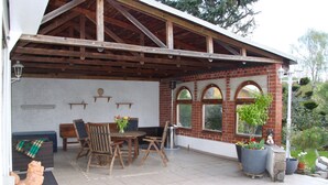 A covered patio with a dining area, brick walls, and potted plants.