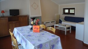 Un salon comprenant un canapé, une table basse, une table à manger avec des chaises, un téléviseur et un élément décoratif mural.