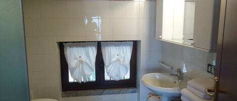 A bathroom with two toilets, a sink, a mirror, and a window with curtains.