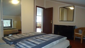Une chambre avec deux lits, une chaise en bois, une cheminée et un miroir au mur.