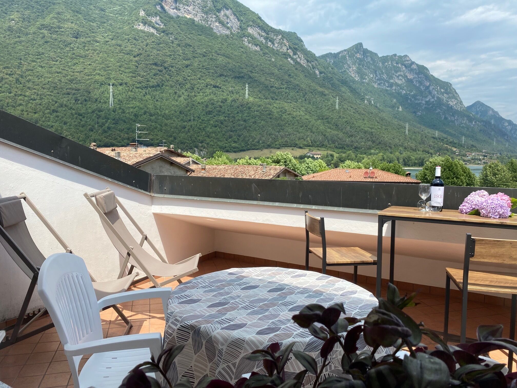 A terrace with a table and chairs, overlooking a mountainous landscape with houses and greenery.