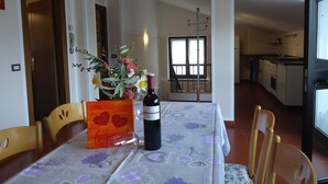 Un coin repas avec une table dressée pour deux personnes, un vase rempli de fleurs et une bouteille de vin.