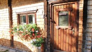 Una puerta de madera con un cartel encima, una ventana con una maceta de flores y un sendero de piedra.