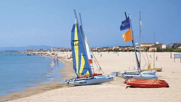 Ein Strand mit Segelbooten und blauem Himmel.